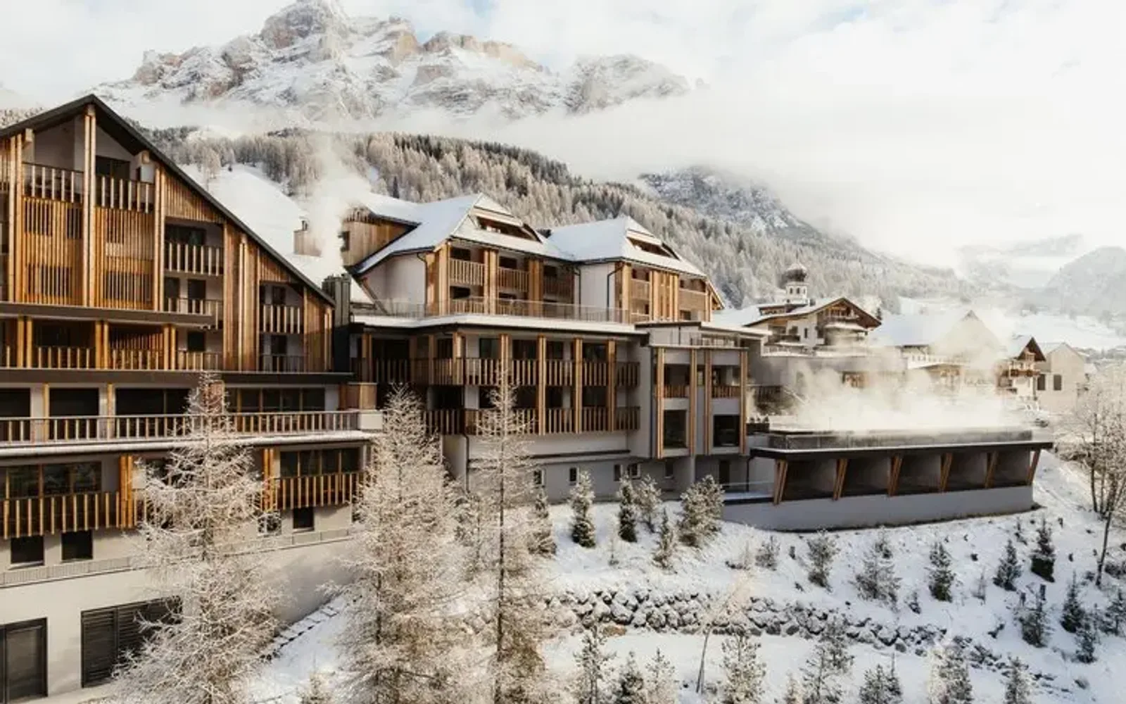 Aman Rosa Alpina exterior with snow-covered Alpine peaks rising behind traditional wooden architecture.