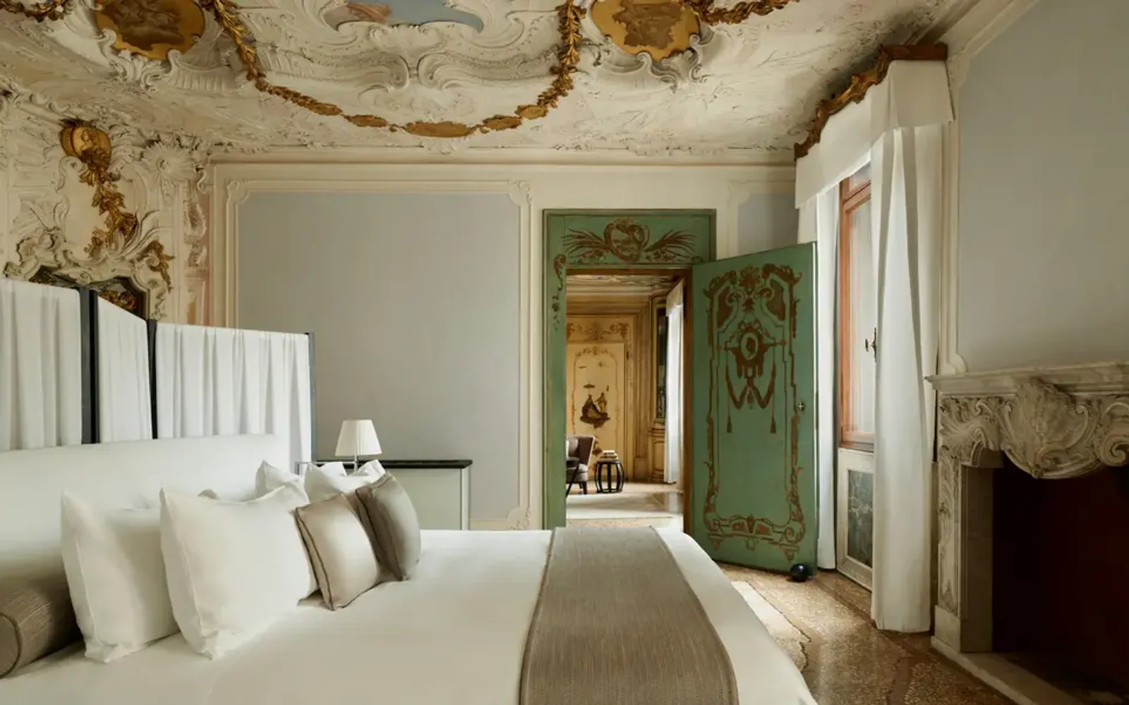 Alcova Tiepolo Suite principal bedroom at Aman Venice, with neutral walls, white bedding, and period architectural details.