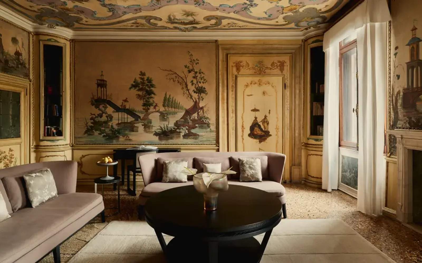 Alcova Tiepolo suite living room at Aman Venice, featuring ornate ceiling frescoes, gilt walls, and classical furnishings.