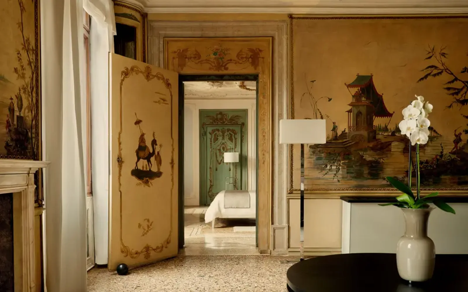 Alcova Tiepolo Suite living room at Aman Venice, with warm wood panelling, doorway to bedroom, and fresh flowers in vase.
