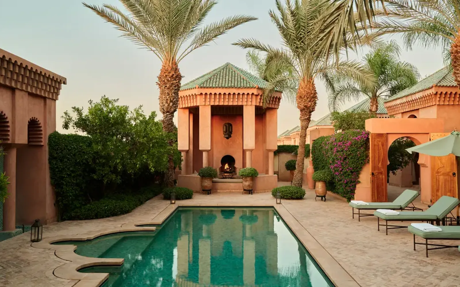 Al Hamra Maison at Amanjena, a terracotta-coloured villa with a reflecting pool and palm trees in a Marrakech riad setting.