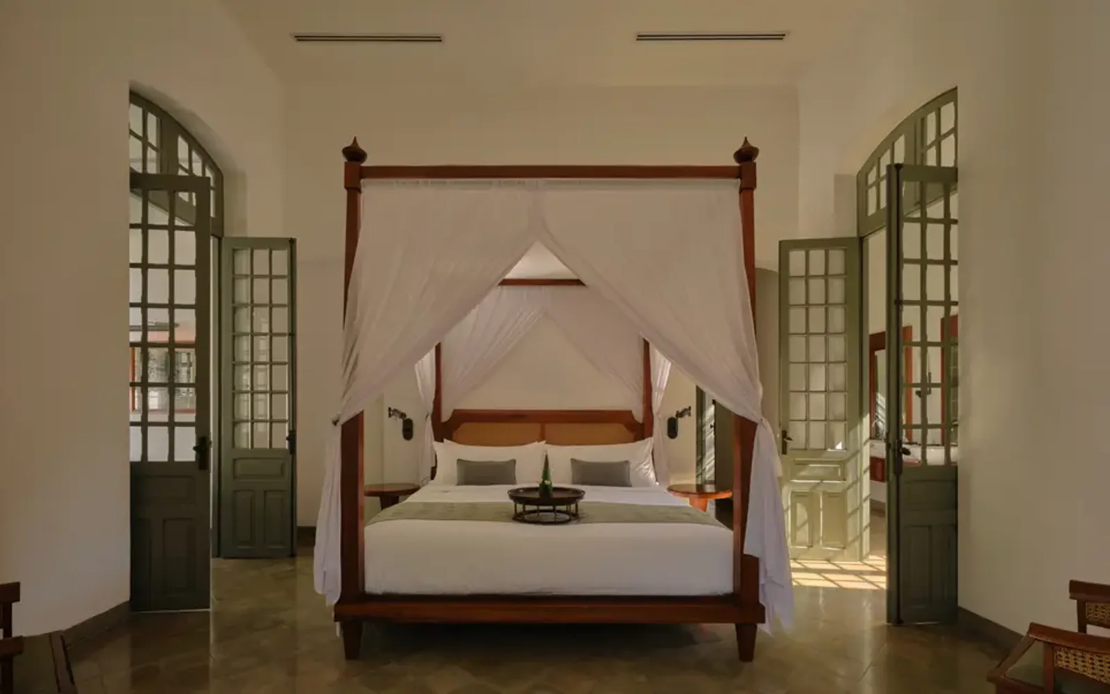 Amantaka principal bedroom with four-poster bed, symmetrical windows, and wooden shutters opening to Mekong views.