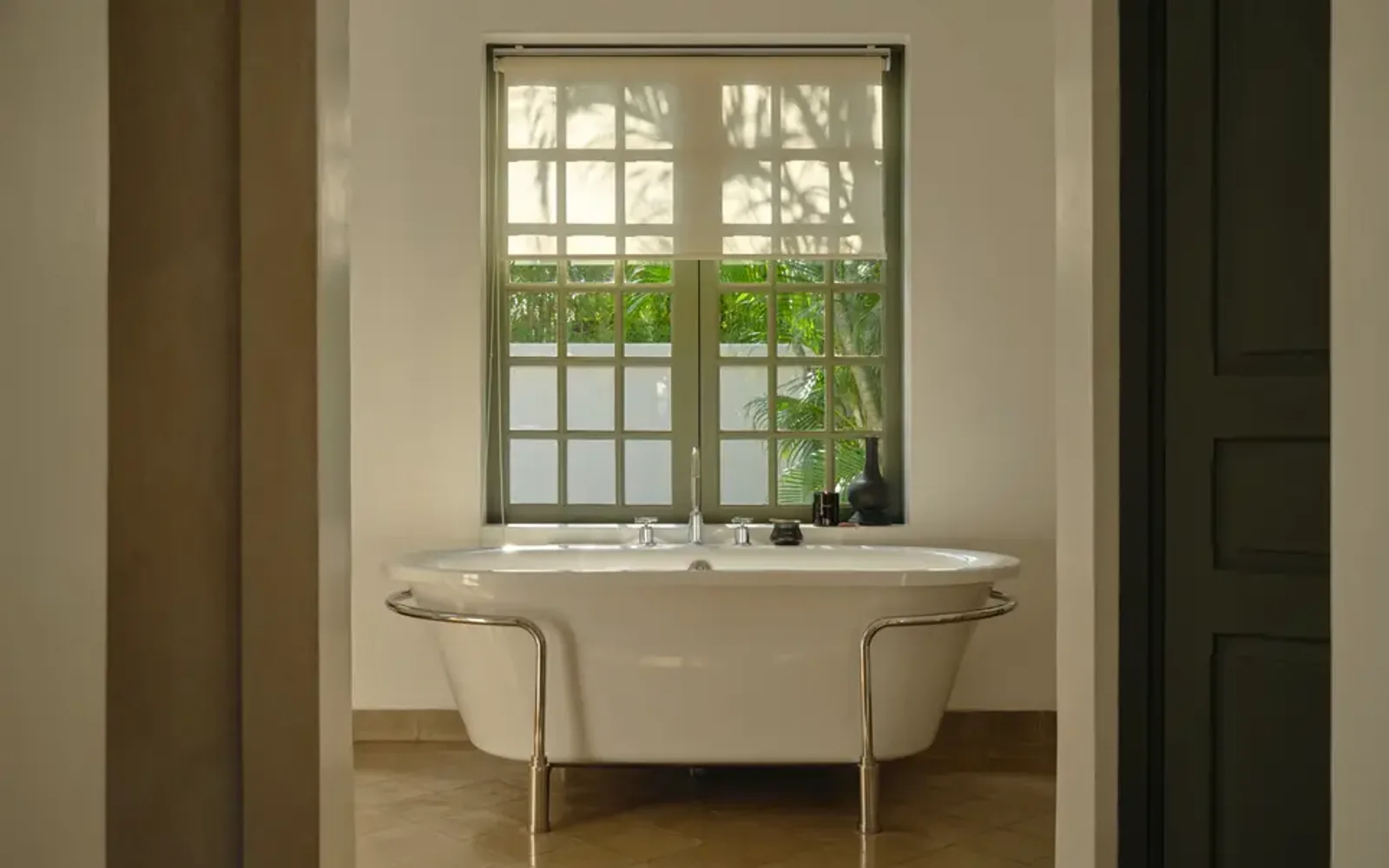 Freestanding bathtub positioned beneath a latticed window at Amantaka, framed by neutral walls and natural light.