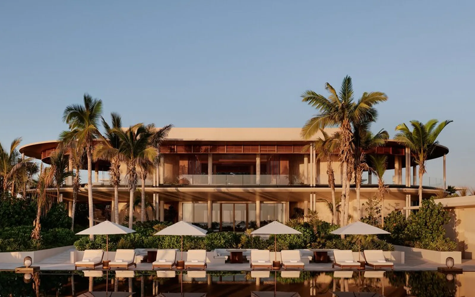 Casa Grande at Amanvari, a sand-coloured residence with palm trees and poolside loungers at sunset, Mexico.