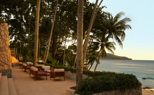 Sunset Terrace at Amanpuri with wooden loungers amongst palm trees overlooking the Andaman Sea at dusk.