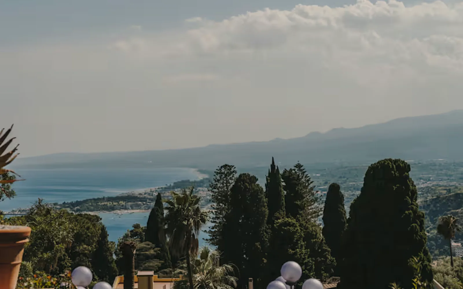View over the hotel garden's rustic mix of flowering shrubs, pines and potted plants, down to the coast and blue Ionian sea.