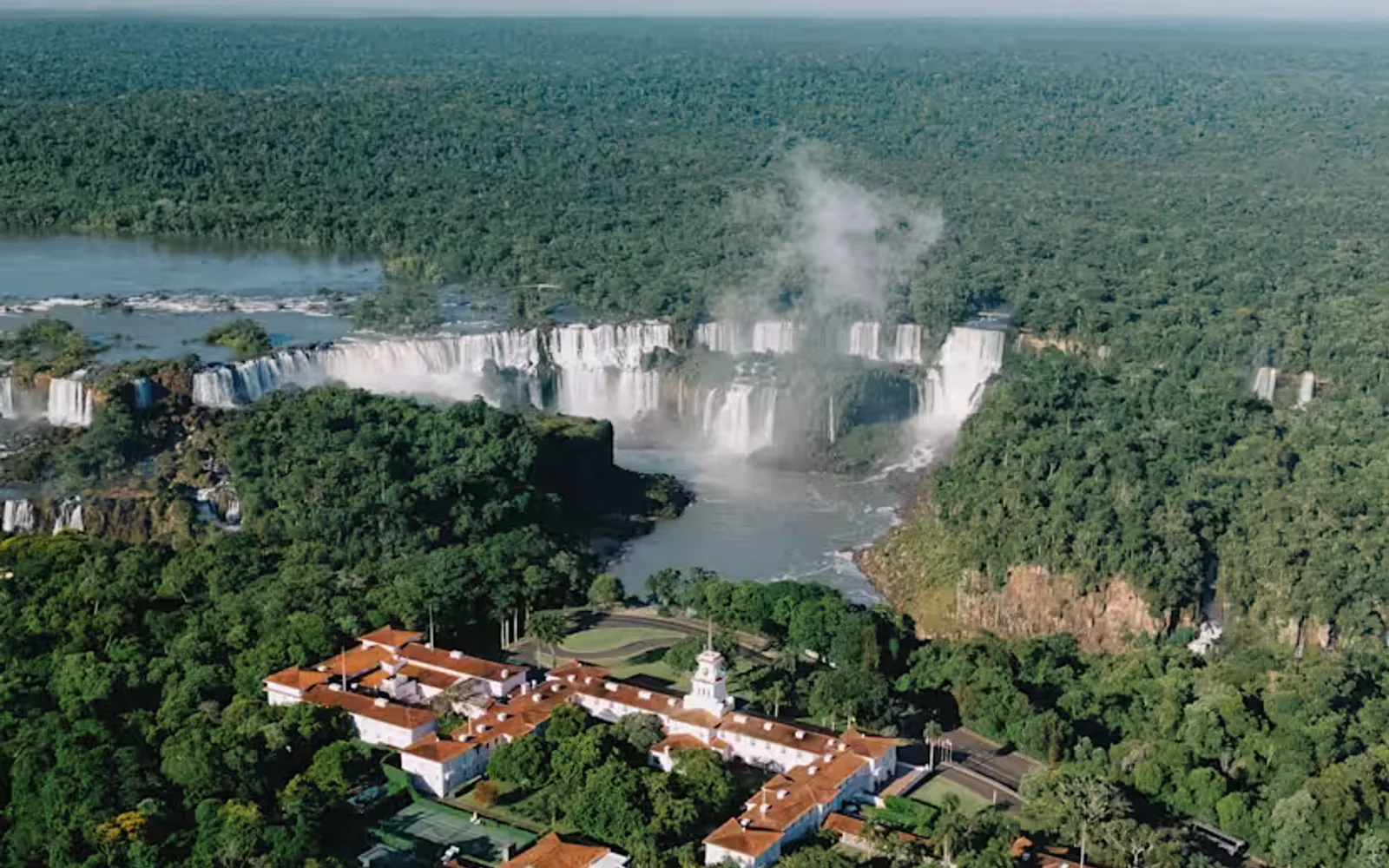 Aerial view of the hotel nestled in dense forest on the banks of the Iguassu facing the horseshoe cascades and plumes of spray.
