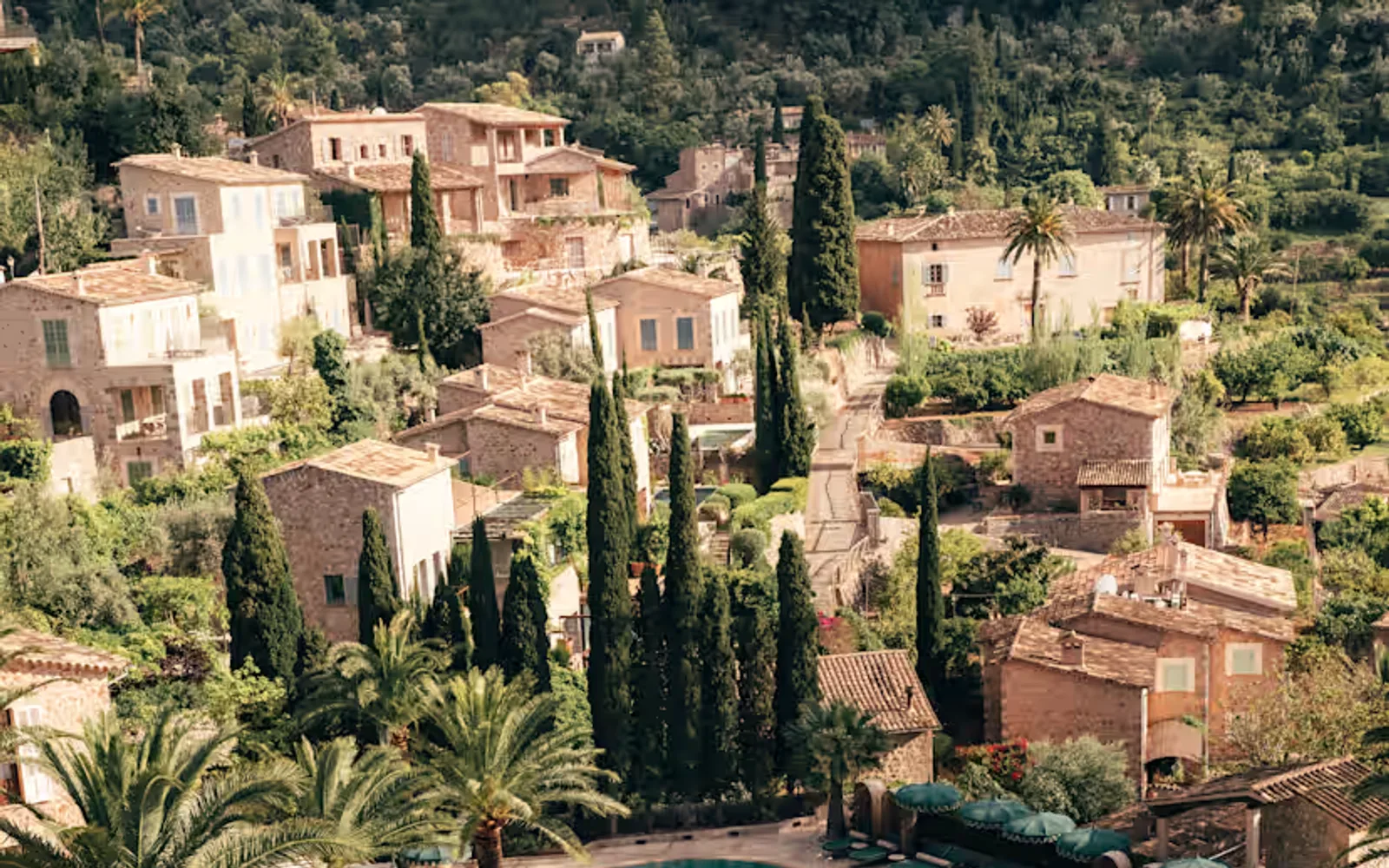 Aerial view of the tropical-shape pool bordered by dark-green parasols and palm trees, overlooked by rustic stone residences.