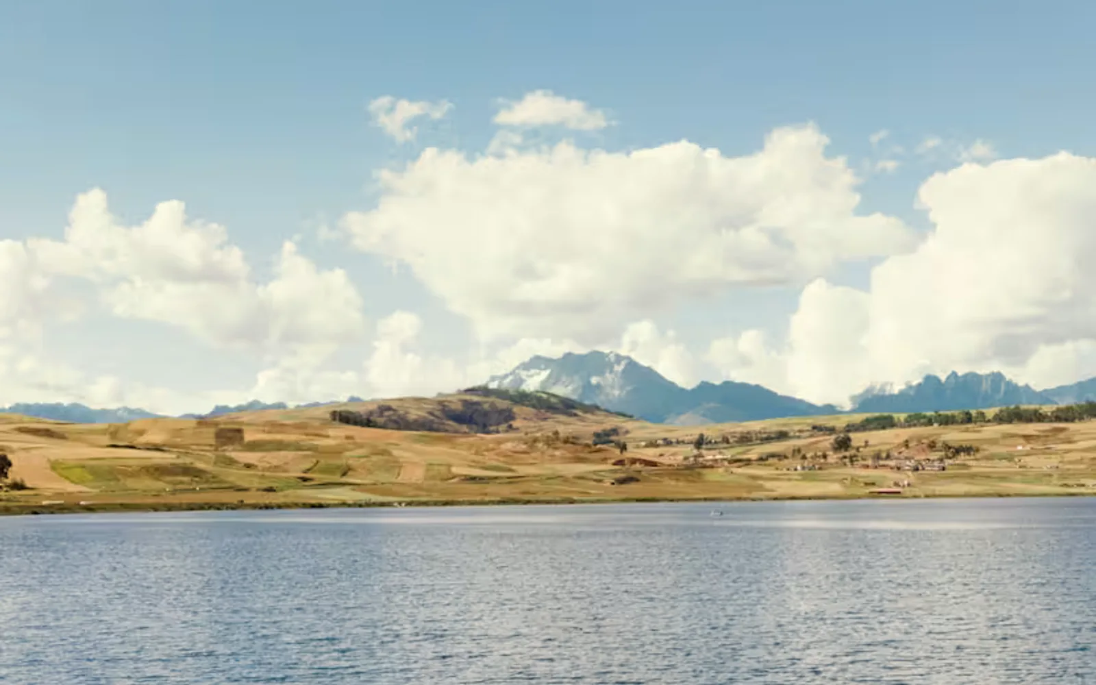 Two people sharing a blue and yellow kayak paddle across the gentle ripples of Lake Huaypo, with a mountain backdrop.