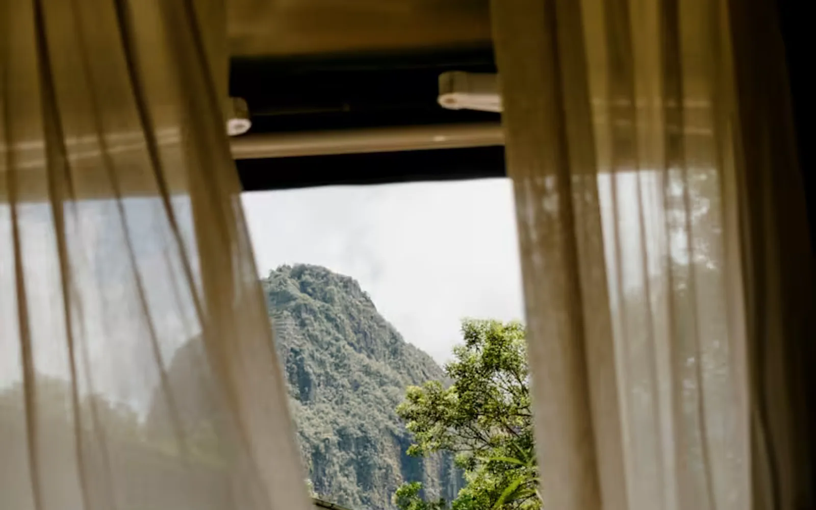 Drapes shift in breeze through a suite door, revealing a view of the imposing Huayna Picchu beyond Sanctuary Lodge's gardens.