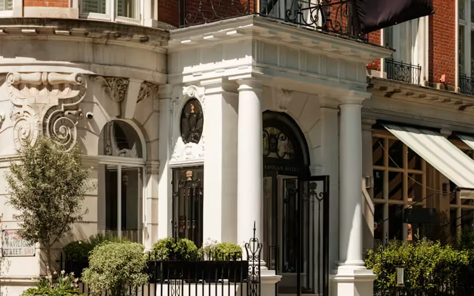 Corner view of The Cadogan Hotel where a branded black flag hangs above the portico entrance set into its Queen Anne façade.