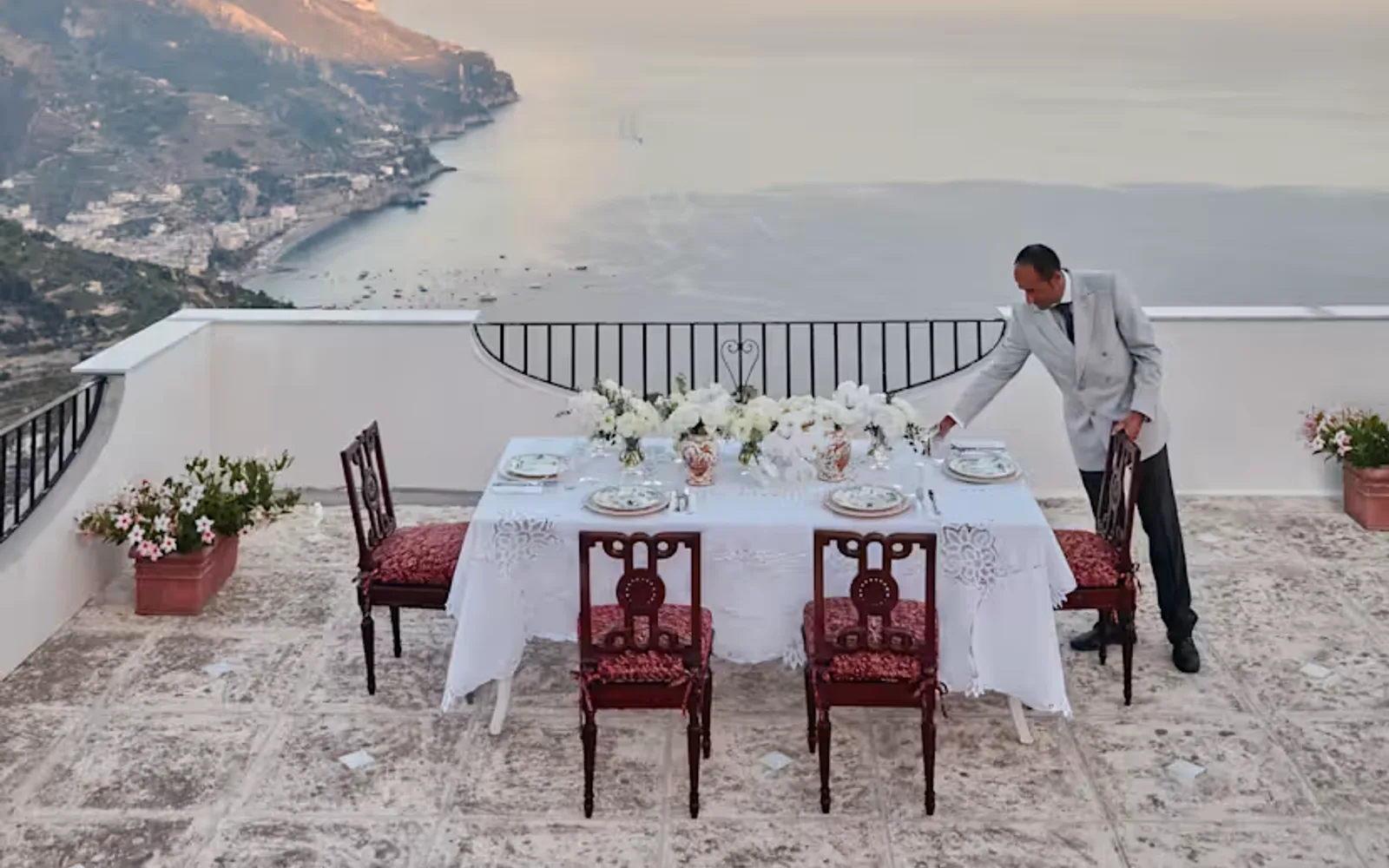 A staff member adds touches to a celebration table with white flowers and sublime coast views on Villa Margherita's terrace.