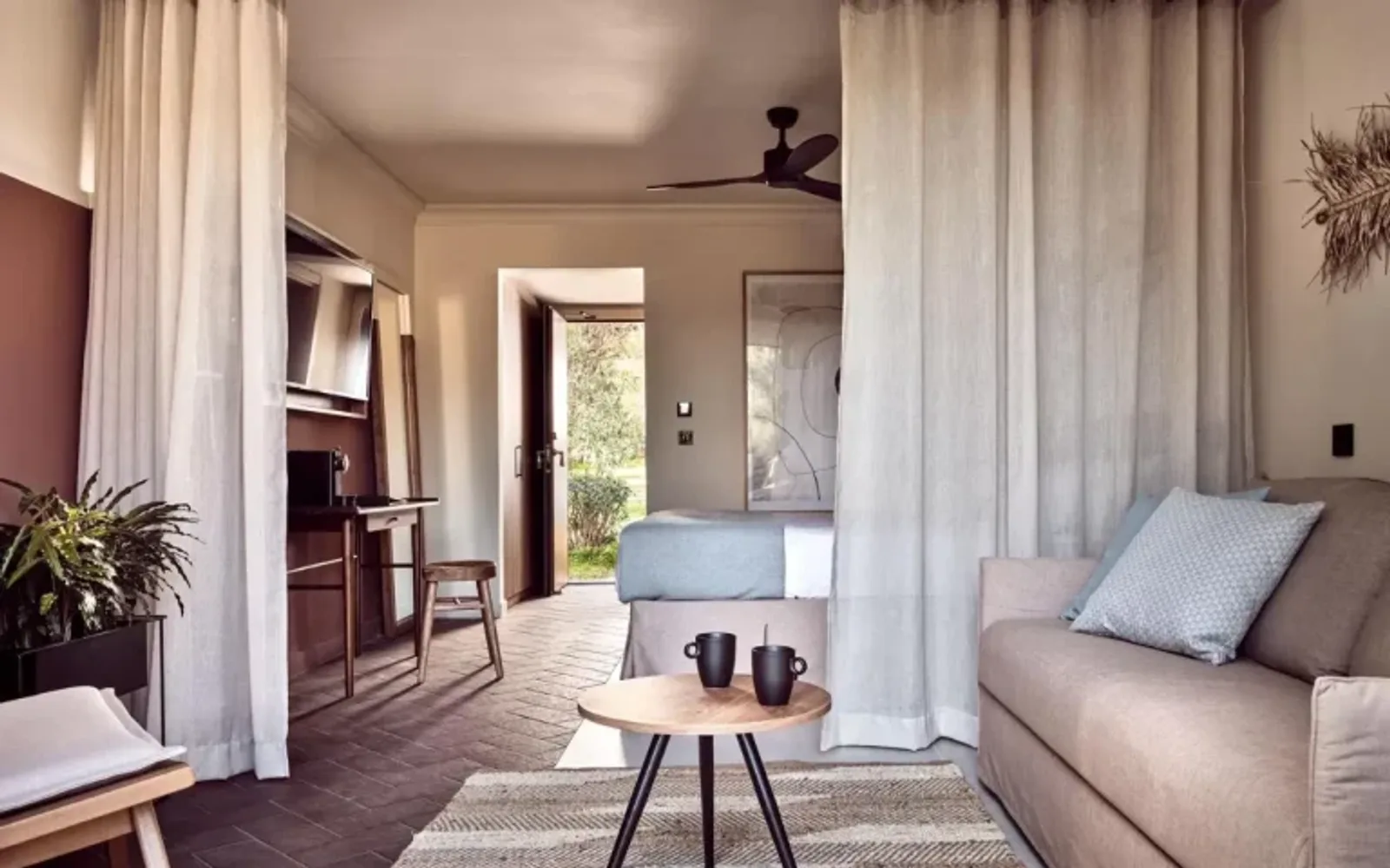 Spacious resort suite interior with living area, work desk, king size bed and garden view at Domes Aulūs Zante family resort