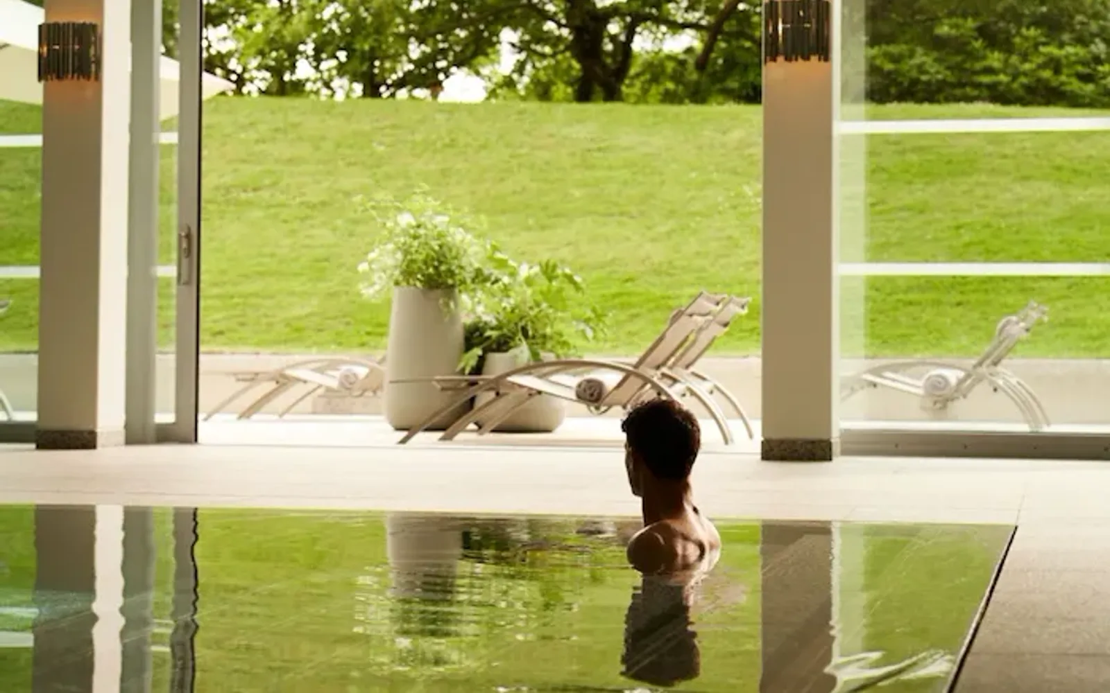 Guests enjoying the pool at Coworth Park with beautfiul light flooding through the open doors to the lush green forest and hills