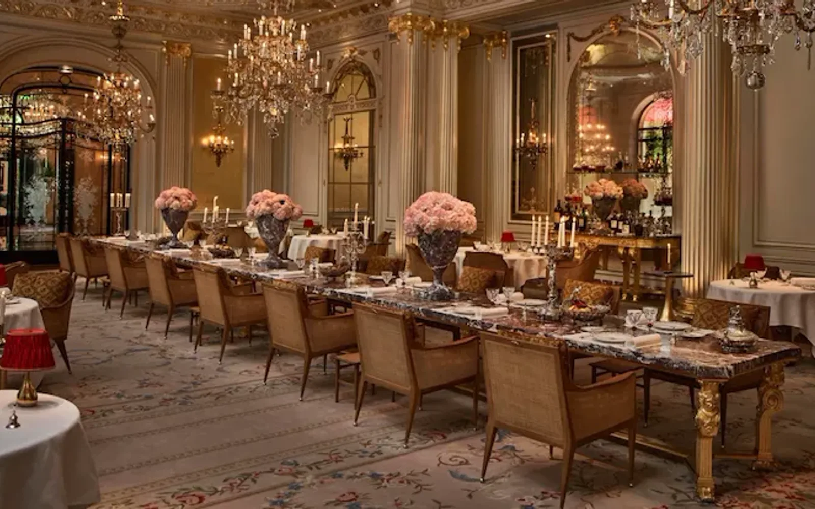 Overview of the Jean Imbert au Plaza Athénée Dining Room and its central marble table with flowers and crystal chandeliers hanging from the ceiling. At Hotel Plaza Athénée, Paris