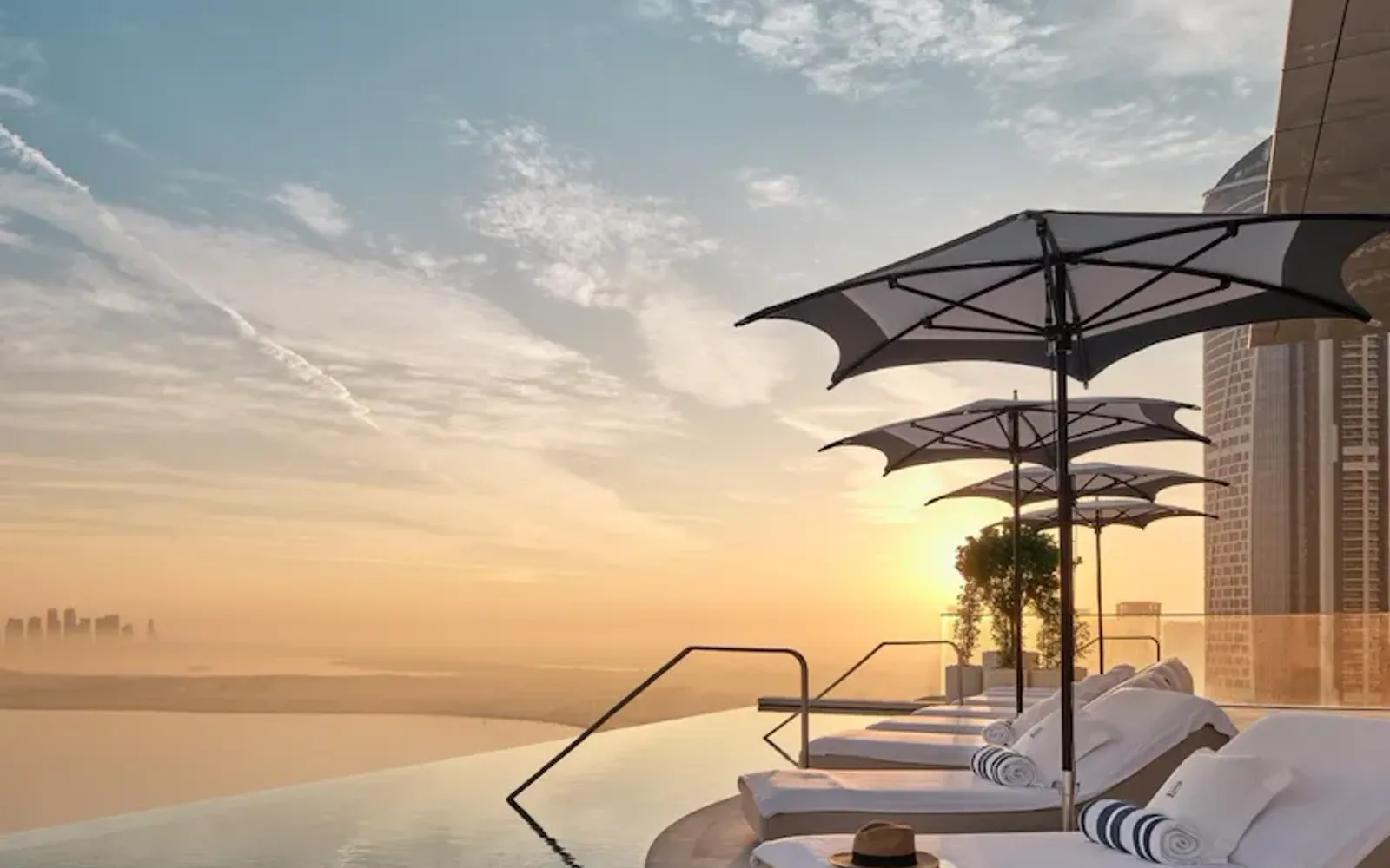 Sunloungers by The Lana's rooftop infinity pool at sunrise with view of Dubai