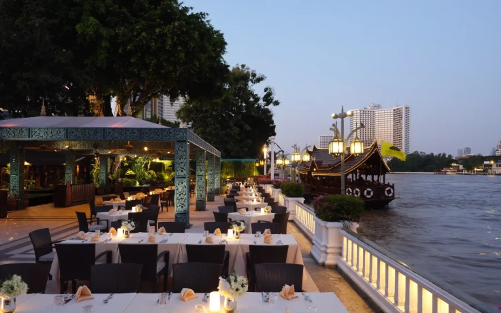 Terrace rim naam outdoor dining at dusk with candlelit tables and hotel boat.