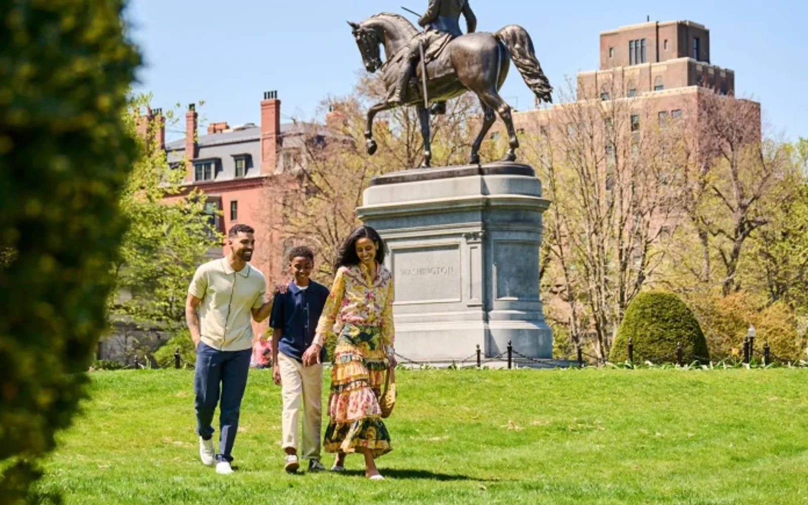 Family strolling through Boston Public Gardens with Washington Statue monument in the background.