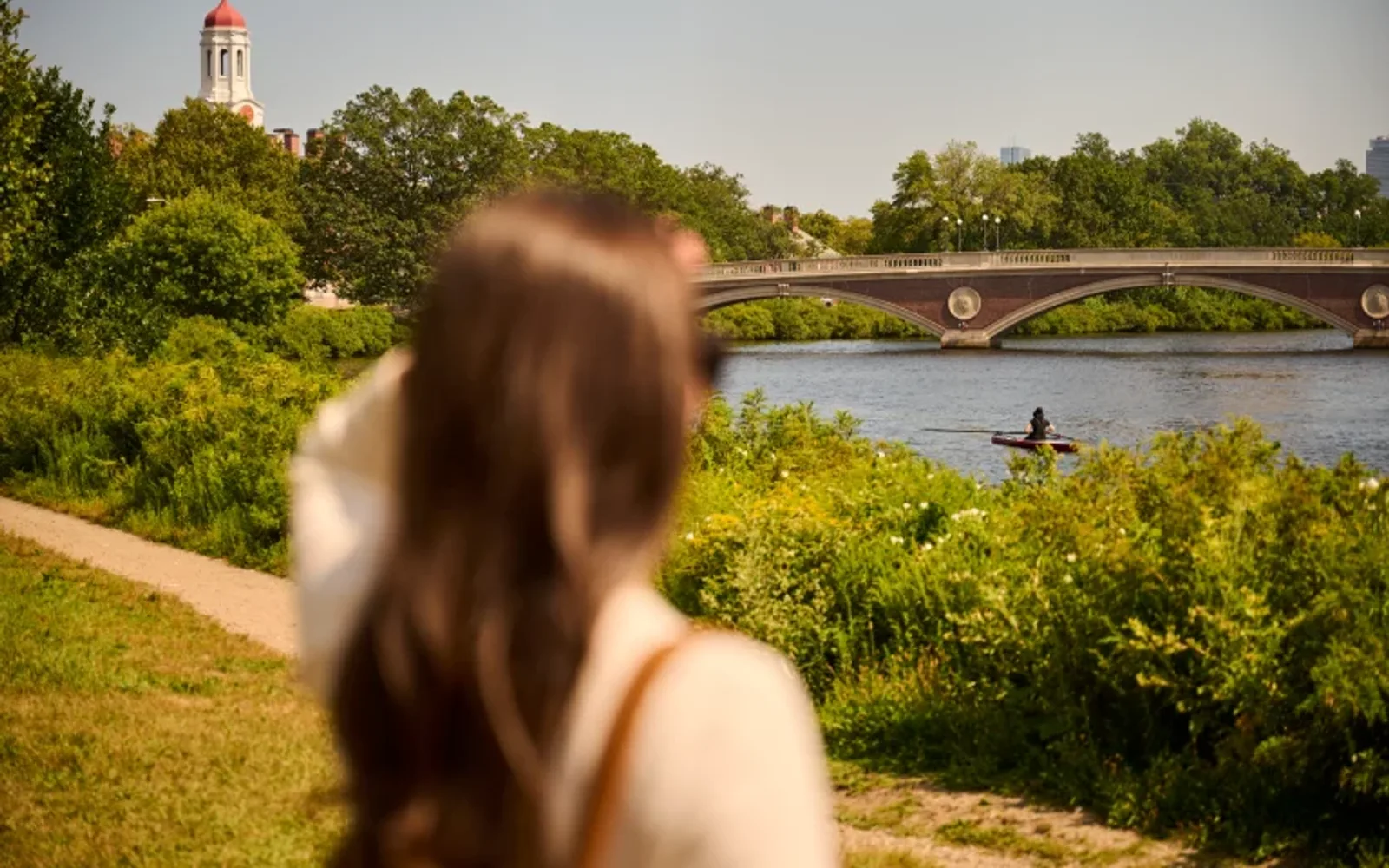 Woman gazing towards the Harvard Bridge in Boston, Massachusetts overlooking the Charles River with a kayaker paddling in background.