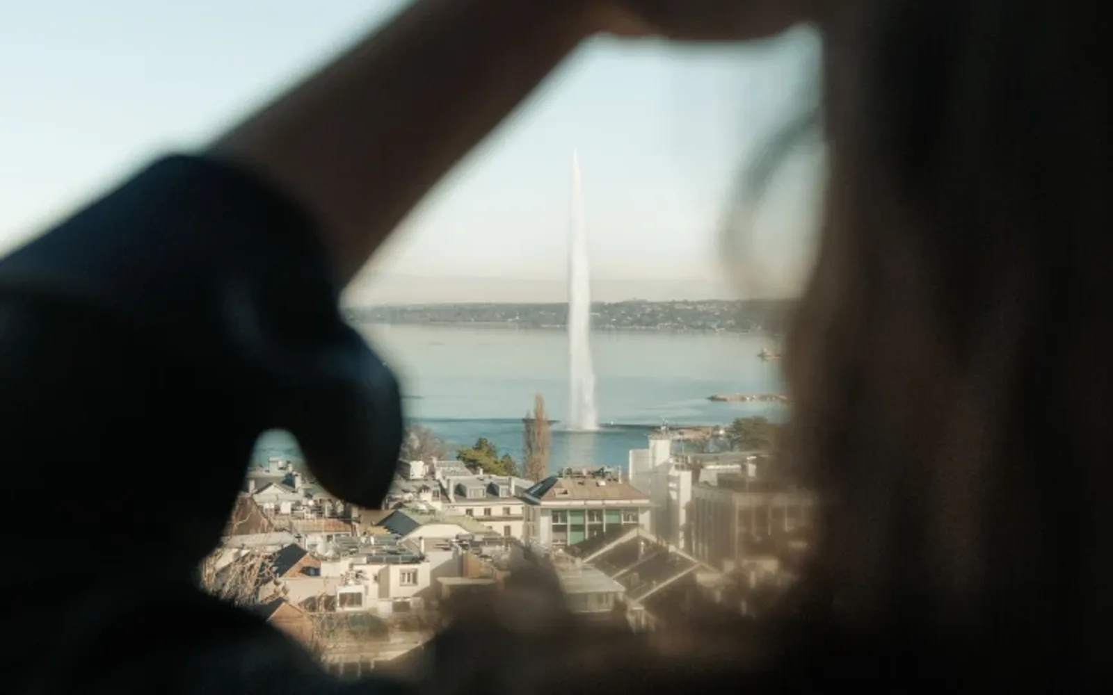 View of Geneva’s Jet d’Eau framed by a softly blurred foreground, overlooking the city and Lake Geneva.