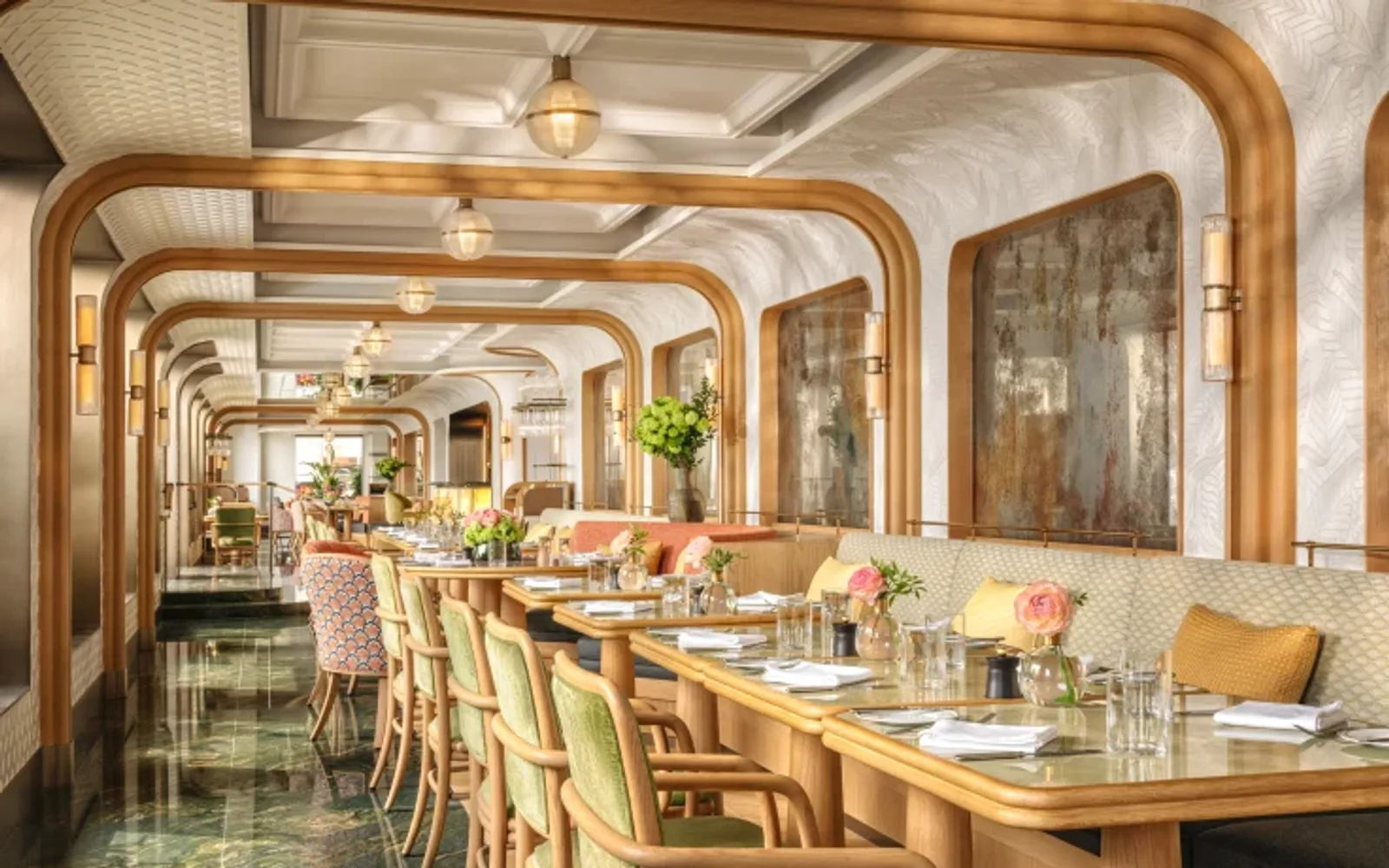 Elegant restaurant interior featuring wooden arch details, green cushioned chairs, and a long table set with glasses and flowers. Warm, inviting ambiance from Terrace Boulud by Mandarin Oriental.