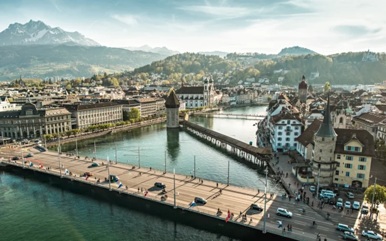 Scenic view of Lucerne’s old town with Chapel Bridge over the Reuss River and alpine mountains in the distance.