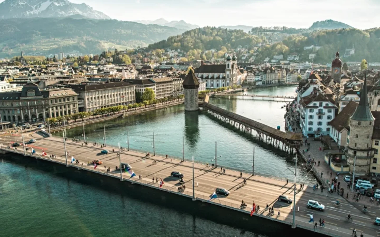 Scenic view of Lucerne’s old town with Chapel Bridge over the Reuss River and alpine mountains in the distance.