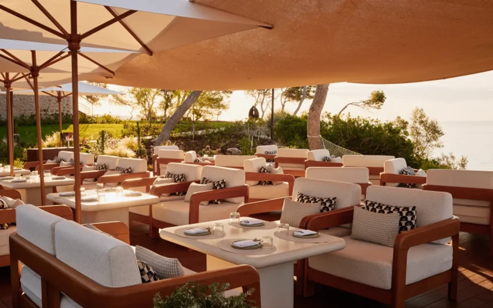 Outdoor terrace dining area with comfortable lounge seating and sea-view surroundings at sunset.