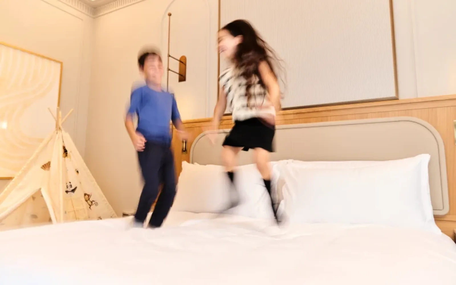 Children jumping on a bed in a luxury hotel suite.